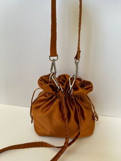 Dimensions H 28 cm/ 11 in  W 22 cm / 8.6 in D 10 cm /  3.9 in Materials Dark bronze  color Satin Fully lined in beige  color satin. Drawstring closure.  Detachable top handle and long strap. Dark bronze satin small bag. The mouth of the bag made of satin  is closed by squeezing.  The handles made of the same satin fabric are mounted on the bag with silver-colored metals. Four metal feet in silver color on the base protect the bag from dirt when placed on the floor. A special material is used bet Gold Handheld Bucket Bag With Removable Pouch, Handheld Gold Bucket Bag With Removable Pouch, Elegant Bucket Pouch For Travel, Evening Bucket Clutch With Detachable Handle, Elegant Brown Pouch With Adjustable Strap, Elegant Brown Pouch With Detachable Strap, Elegant Bucket Travel Pouch, Elegant Bucket-shaped Travel Pouch, Chic Evening Bucket Pouch