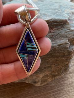 This beautifully well crafted Diamond shape Pendant has been handmade by a Navajo Artisan. The Colors of the Pendant come from Lapis Lazuli, Turquoise and Blue Opal. The Pendant measures 2.25” long and 3/4” wide. There are two pendants available and the design will vary. “Winds of Wisdom” (Lapis Lazuli, Turquoise and Blue Opal. The Navajo (Dine’) believe that the wind is a powerful source. The native tradition believes that at any moment, the blowing wind can inspire one with hope, resolve, and Artisan Blue Inlay Necklaces, Unique Blue Necklace With Inlay, Blue Sterling Silver Necklace With Inlay, One-of-a-kind Blue Turquoise Spiritual Necklace, Southwestern Blue Necklace With Inlay, Southwestern Blue Gemstone Necklace, Southwestern Blue Inlay Necklace, Traditional Turquoise Inlay Necklace As Gift, Traditional Turquoise Necklace With Inlay For Gift