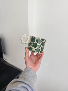 a person holding a coffee cup in front of a wall with a flower design on it