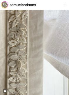 an embroidered curtain hanging on the side of a window with white sheer curtains behind it