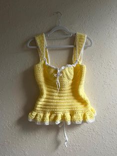 a yellow crocheted dress hanging on a wall next to a white hanger