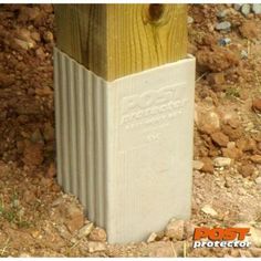 a wooden post sitting on top of a dirt field next to grass and rocks,