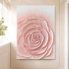 a pink rose on a white wall next to a window