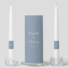 two white candles sitting next to each other on top of a glass stand with the words charlotte grace's birth printed on it