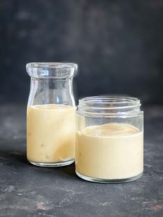 a glass jar filled with yellow liquid next to a container full of white liquid on a black surface