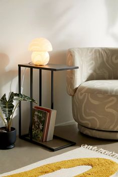 a living room with a chair, lamp and books on the floor in front of it