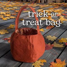 an orange trick or treat bag sitting on top of a wooden floor covered in leaves