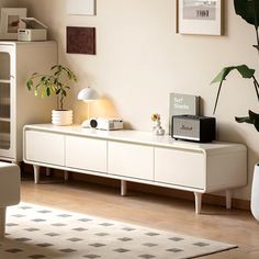 a living room with white furniture and plants on the sideboard in front of it