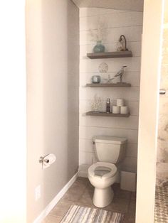 a white toilet sitting inside of a bathroom next to a shelf filled with vases