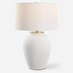 a white table lamp with a beige shade on the base and a gold trim around the top