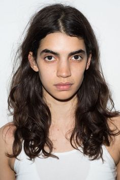 a young woman with long hair wearing a white tank top and looking at the camera