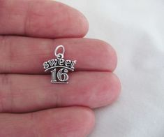 someone is holding a small silver charm with the number sixteen on it's side