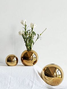 three gold vases with flowers in them on a white table cloth next to each other