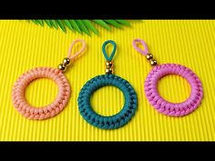 three different colored rope earrings sitting on top of a yellow table next to palm leaves