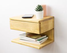 a wooden shelf with two books and a phone on it, next to a wall mounted succulent plant