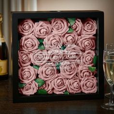 a black box with pink roses in it next to two champagne glasses and a bottle