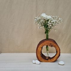 a vase filled with white flowers sitting on top of a wooden table next to rocks