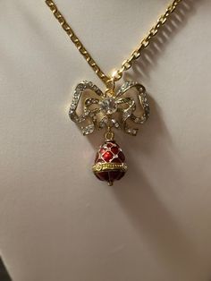 From the world renowned Romanov Gifts Co, we bring you the last available stock of the iconic brand.  Imperial Trellis Egg & Bow Necklace, in beautiful Ruby Red. The necklace is cast of bronze, with 18K yellow gold-plated accents. Set with Austrian Crystal gemstones, this pendant features a translucent enameling of ruby red. The chain is 18 inches in length. The total necklace measures approximately 2 in. height. The chain has an authentic hallmark "Faberge" tag, with the initials "I.F." engrave Red Pendant Necklace For Christmas, Elegant Holiday Necklaces For Celebrations, Elegant Holiday Gift Necklaces, Red Costume Jewelry Necklace For Gift, Vintage Gold Jewelry For Holidays, Vintage Red Jewelry For Holidays, Vintage Necklace For Christmas Gift, Vintage Necklaces For Christmas Gifts, Red Vintage Jewelry For Holidays