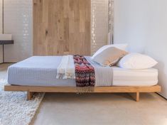 a bed with white sheets and pillows in a room next to a wooden headboard