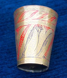 a gold colored cup with red and blue designs on the inside sits on a blue surface