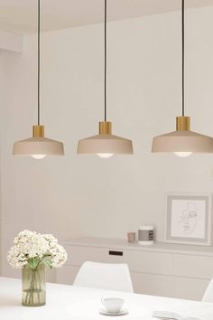 three lights hanging over a white table with flowers in a vase on the dining room table