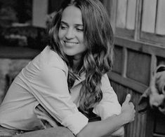 a black and white photo of a woman sitting on a bench with a dog in the background