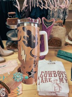 a person holding up a travel mug in front of some other items on a table