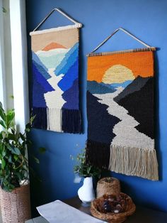 two woven wall hangings on a blue wall next to a potted plant and vase