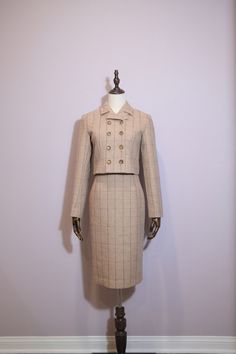 Features: - Elegant beige plaid fabric with subtle lines. - Six decorative buttons in two rows on the jacket. - Cropped jacket for a contemporary twist on a classic style. - High-waisted pencil skirt to elongate and enhance your silhouette. - Perfect balance of vintage charm and modern sophistication. - Versatile style suitable for a variety of occasions. Composition: 80% Wool 20%Polyester Care: Suggested dry clean only to maintain fabric integrity. Fitted Buttoned Formal Skirt, Formal Fitted Skirt With Buttons, Elegant Beige Buttoned Skirt, Elegant Beige Skirt With Buttons, Classic Fitted Beige Skirt Suit, Classic Beige Fitted Skirt Suit, Beige Fitted Skirt Suit For Fall, Beige Plaid, High Waisted Pencil Skirt