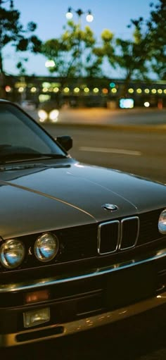 a black car is parked on the side of the road at night with street lights in the background