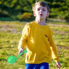 a young boy holding two green plastic spoons in his left hand and wearing a yellow sweater