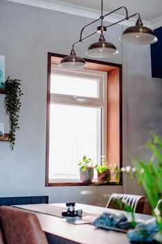 a dining room table with chairs and potted plants on the window sill next to it