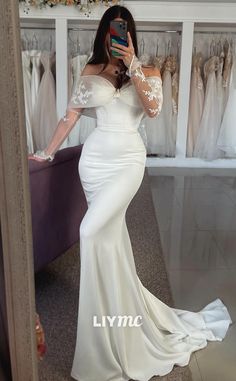 a woman taking a selfie in front of a mirror wearing a white gown and holding a cell phone