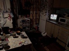 a messy kitchen with an old tv on the wall and many clutters all over the table