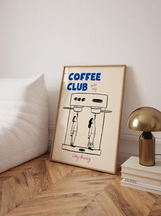 a coffee club poster sitting on top of a wooden floor next to a lamp and pillow