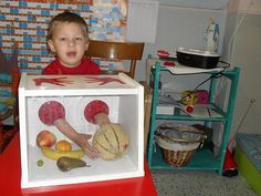 a young boy sitting in a toy refrigerator with fruits and veggies inside it