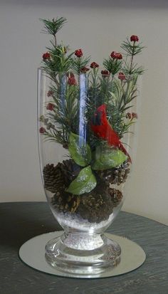 a glass vase filled with plants and pine cones