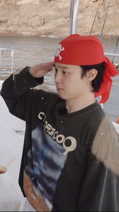 a young boy wearing a red bandana on top of his head while standing next to a boat