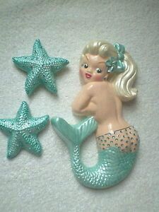 two little mermaid figurines sitting next to each other on a white sheet with blue stars