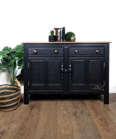 a black sideboard with brass handles and two plants on top, in front of a white wall