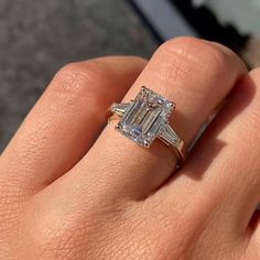 a woman's hand holding an engagement ring with two baguettes on it