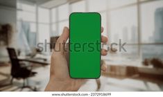 a person holding up a green cell phone in an office with large windows and desks