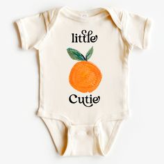 a white baby bodysuit with an orange on the front and words little cutie