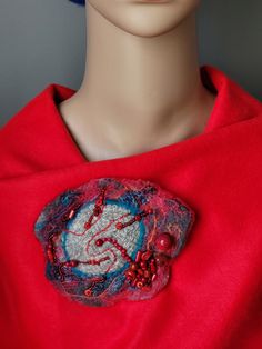 a mannequin head wearing a red shirt with a dragon brooch on it