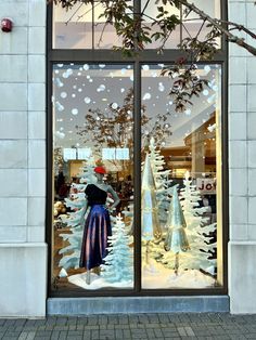 a store front window with mannequins dressed in winter clothes and snow trees