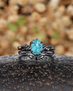 a turquoise stone ring sitting on top of a black piece of rock with leaves around it