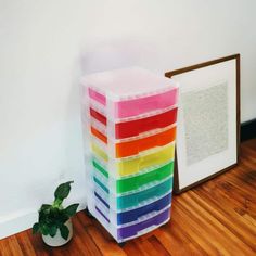 a stack of multicolored plastic storage boxes next to a potted plant on the floor