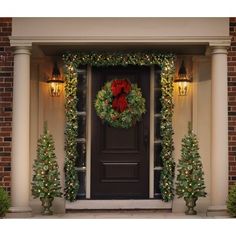 a christmas wreath on the front door of a house decorated with lights and garlands