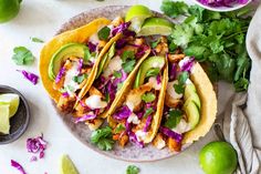 three tacos with shredded cabbage, avocado and cilantro on the side