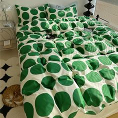 a cat laying on the floor next to a bed with green polka dot sheets and pillows